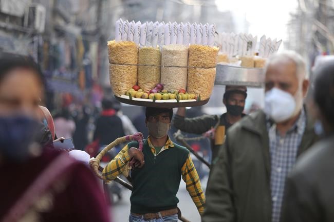 A snacks vendor wears a face mask as a precaution against COVID-19 and walks in a market area in Jammu, India, Saturday, Nov. 27, 2021. (AP Photo/Channi Anand)