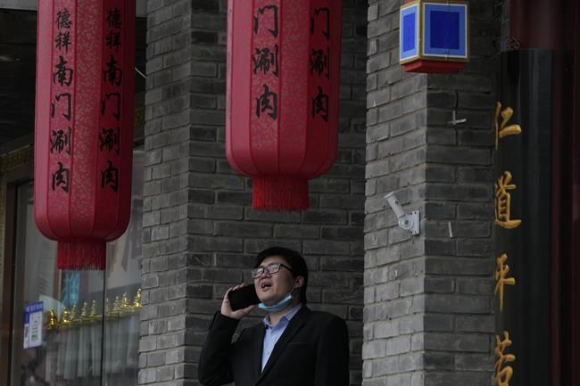 A man lowers his mask to speak on his phone outside a restaurant in Beijing, China, Monday, Nov. 29, 2021. As cases of a new coronavirus variant are confirmed around the world, an increasing number of countries are tightening their borders as fear spreads of yet another extension of pandemic suffering. (AP Photo/Ng Han Guan)