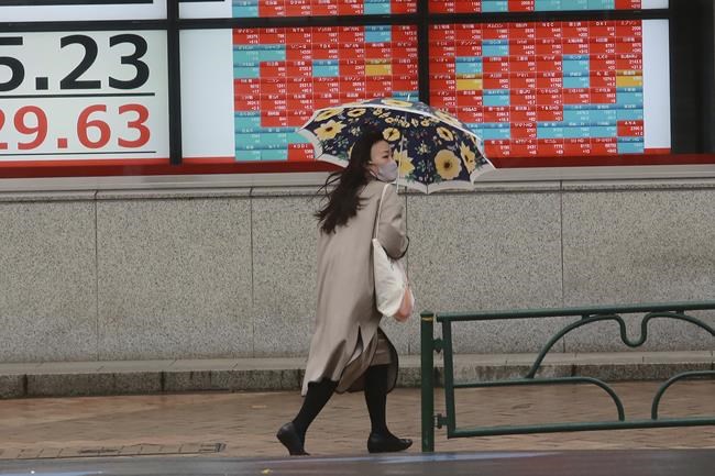 A woman walks by an electronic stock board of a securities firm in Tokyo, Wednesday, Dec. 8, 2021. Stocks advanced Wednesday in Asia after another broad rally on Wall Street as investors wagered that the new variant of the COVID-19 virus won’t pose a big threat to the economy. (AP Photo/Koji Sasahara)