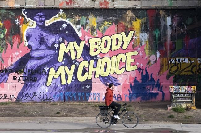 A person goes by bike along the Danube Canal during the lockdown in Vienna, Austria, Tuesday, Dec. 7, 2021. A graffiti on the wall in the back says ‚my body, my choice'. (AP Photo/Lisa Leutner)